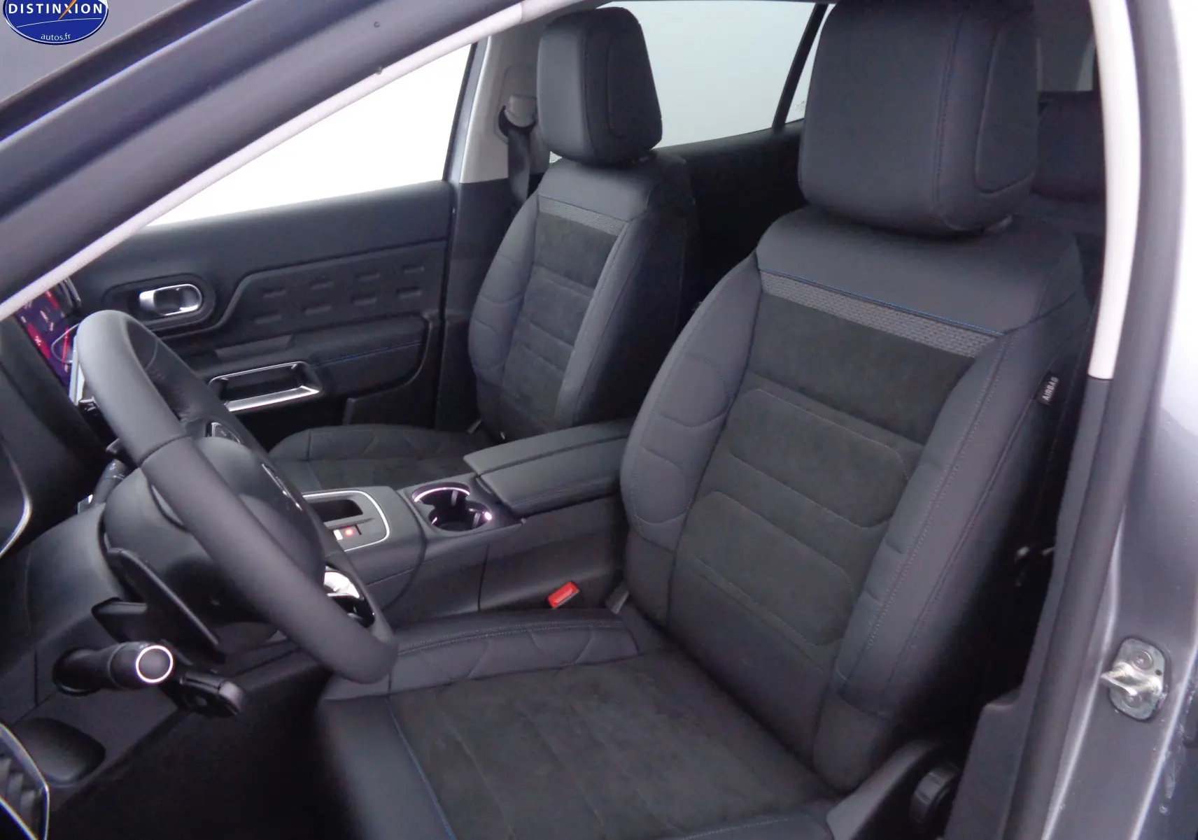 Vue intérieure côté conducteur du Citroën C5 Aircross gris Artense, sièges en cuir noir avec surpiqûres bleues et console centrale.
