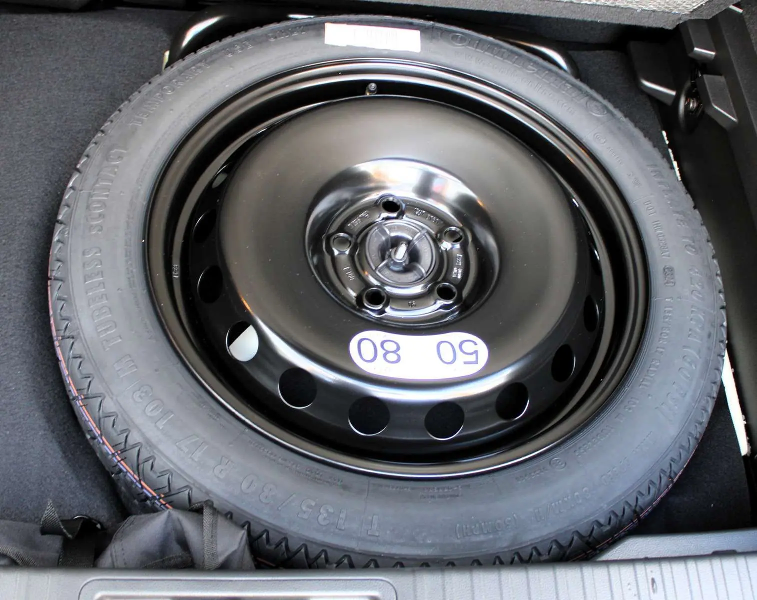 Roue de secours noire en gros plan dans le coffre d'un Renault Captur 2025 hybride noir métal avec toit gris.