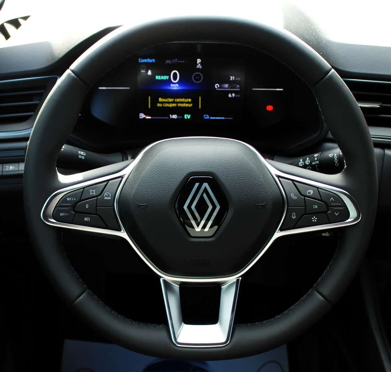 Volant noir du Renault Captur 2025 hybride avec commandes intégrées et tableau de bord numérique en arrière-plan.