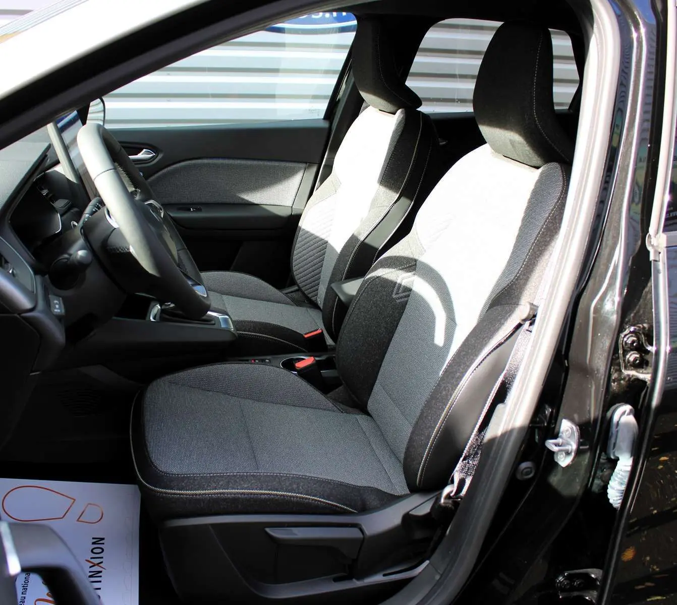 Intérieur du Renault Captur 2025, sièges bi-ton gris clair et foncé, vue côté conducteur porte ouverte.