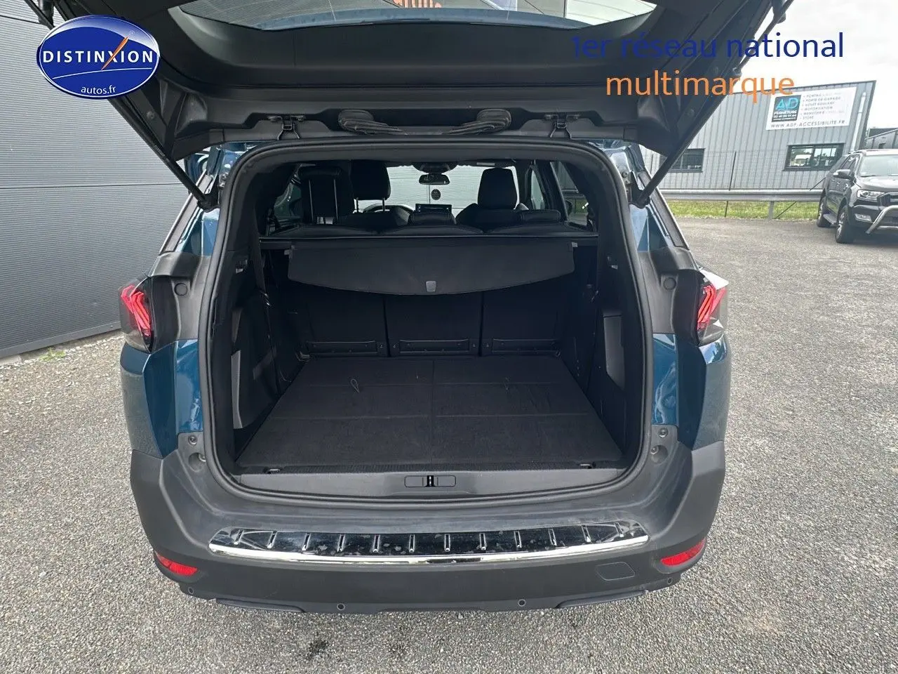 Coffre ouvert d'un Peugeot 5008 bleu vu de l'arrière, montrant l'espace de chargement et la banquette arrière.