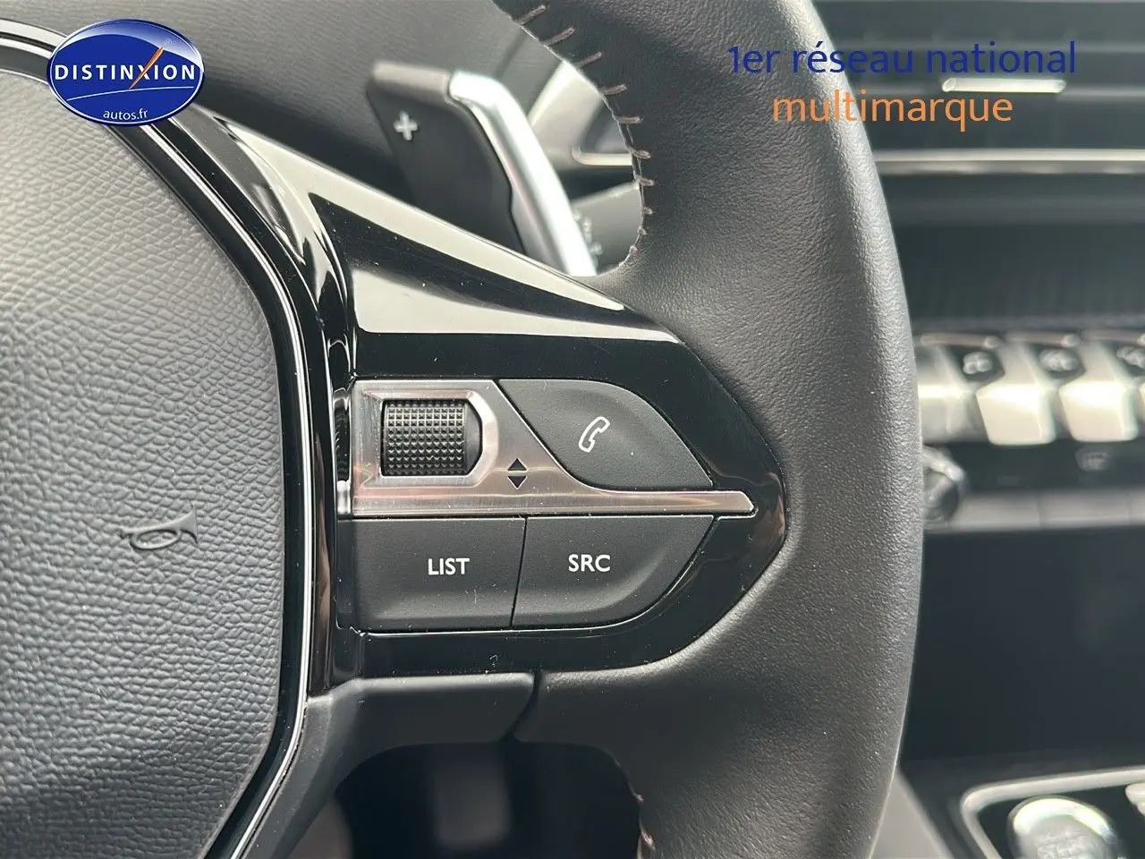 Gros plan sur les commandes gauche du volant cuir noir du Peugeot 5008 2024 avec tableau de bord en arrière-plan flou.