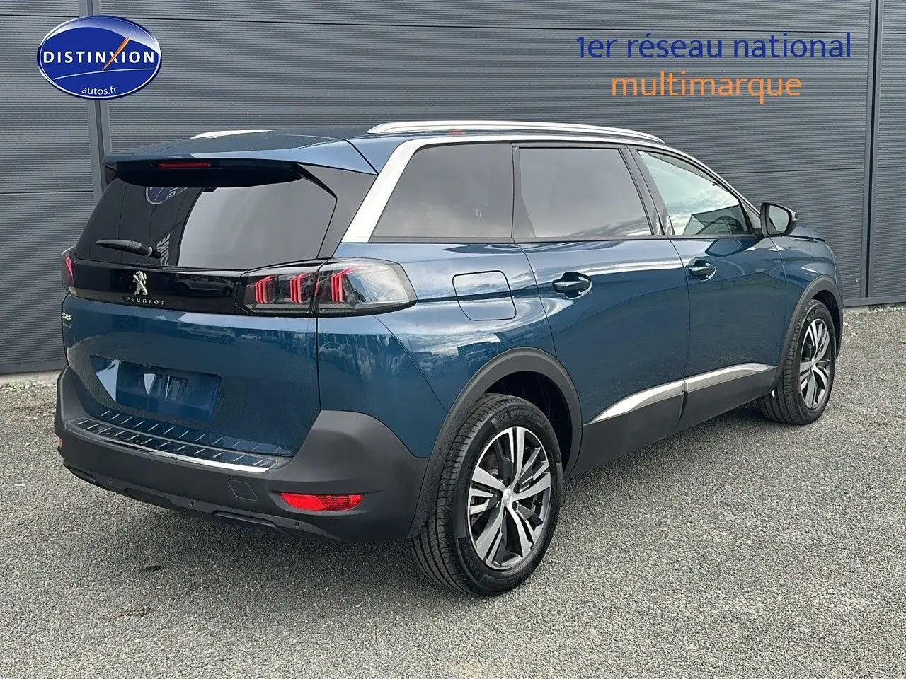 Vue 3/4 arrière droite d'un Peugeot 5008 bleu 2024 avec jantes alliage 18 pouces et vitres surteintées.