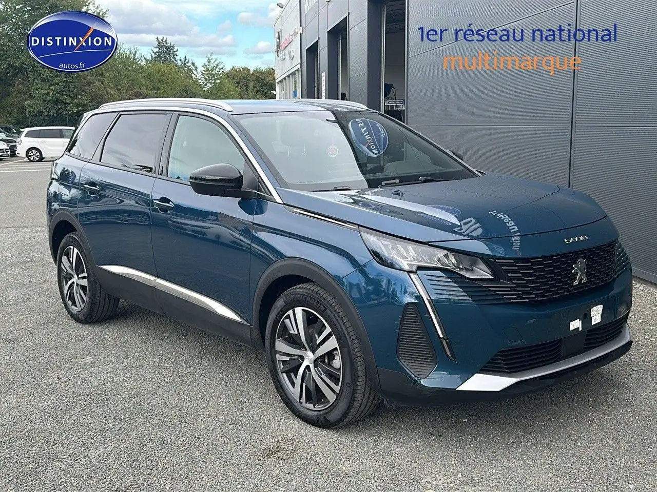 Peugeot 5008 bleu en 3/4 avant droit, avec calandre à damiers chromés et jantes alliage 18 pouces visibles.