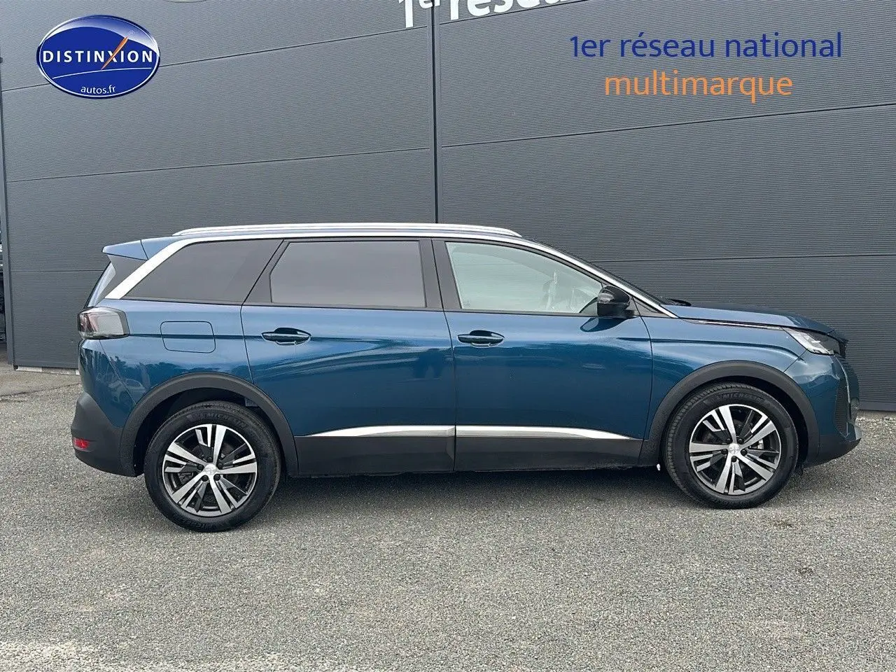Profil droit d'un Peugeot 5008 bleu 2024 avec jantes alliage et vitres teintées sur fond gris.