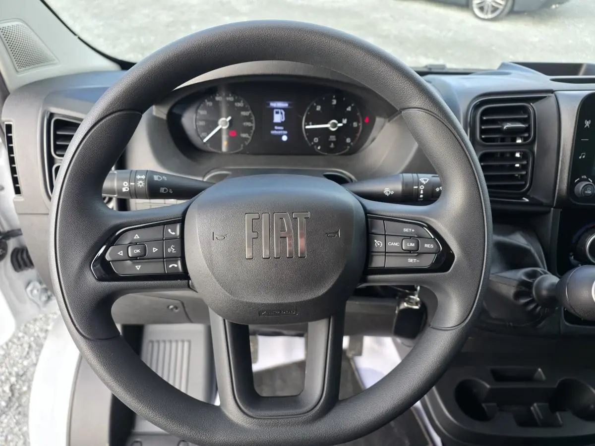 Vue intérieure centrée sur le volant et la console centrale du Fiat Ducato Fourgon blanc, avec levier de vitesse manuel.