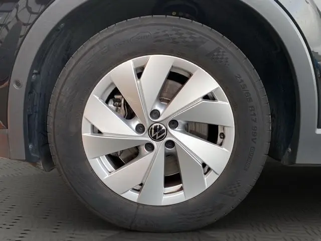 Gros plan sur la roue avant droite du Volkswagen Tiguan noir 2024, mettant en valeur la jante en alliage argentée.