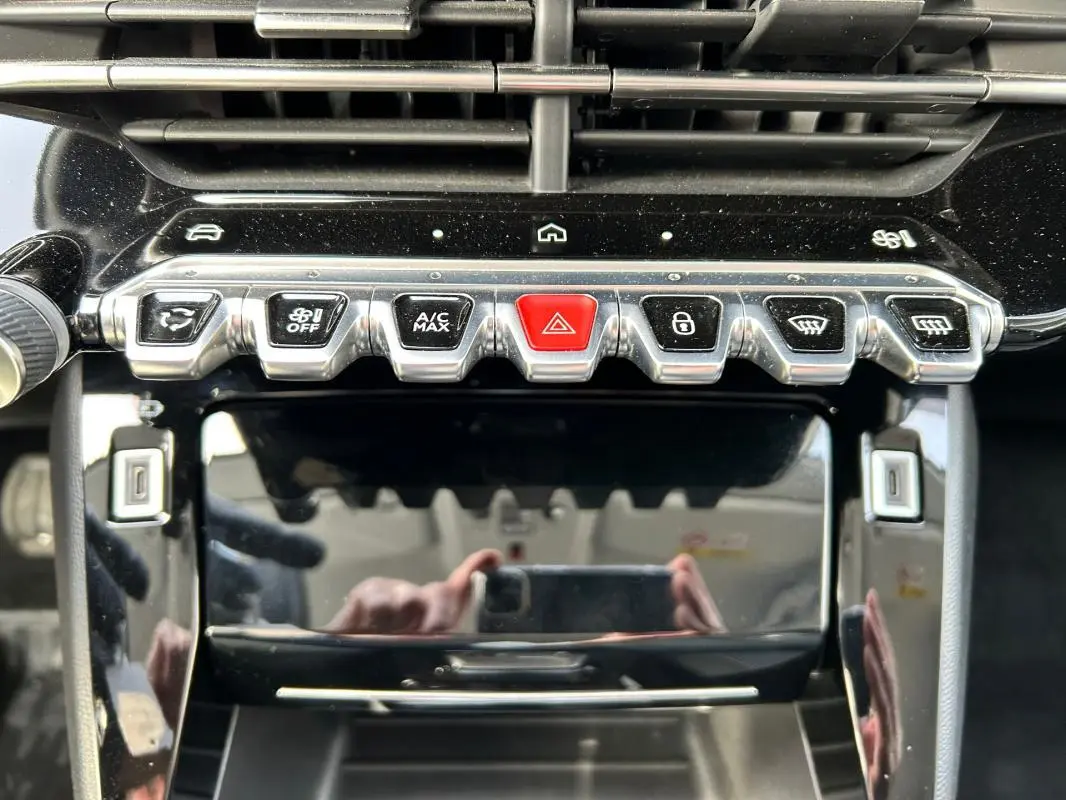 Gros plan sur la rangée de boutons de commande chromés avec bouton rouge d’alerte au centre, tableau de bord Peugeot 208 Hybrid 2024.