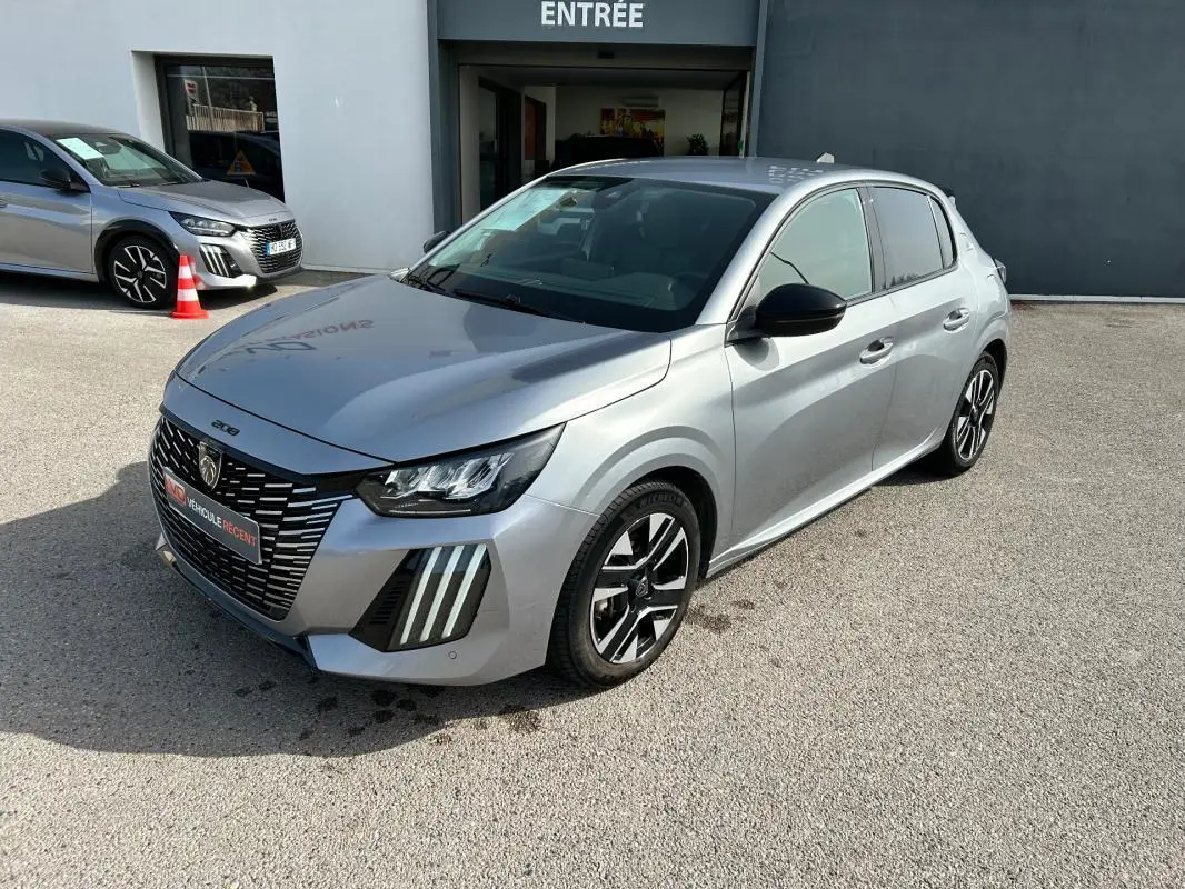 Peugeot 208 Hybrid gris vue 3/4 avant droit, avec calandre noire distinctive et jantes alliage bicolores.