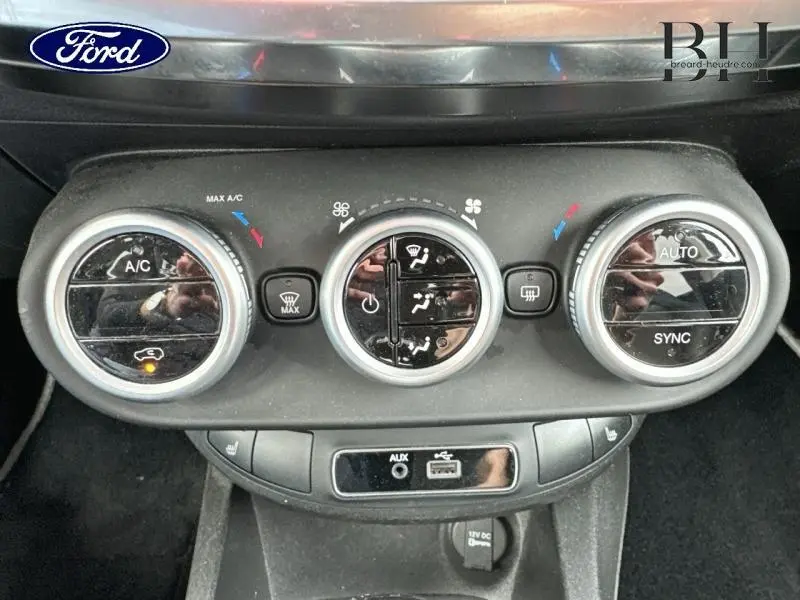 Gros plan sur les commandes de climatisation automatique de la FIAT 500X noire, avec boutons circulaires et prises AUX/USB.