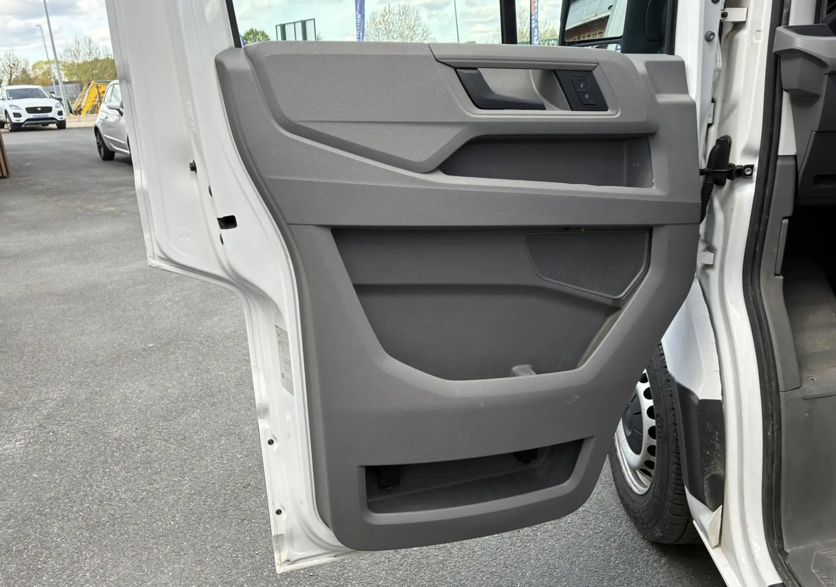 Vue rapprochée de la porte latérale droite ouverte d’un Volkswagen Crafter blanc, montrant le panneau intérieur gris avec rangements intégrés.