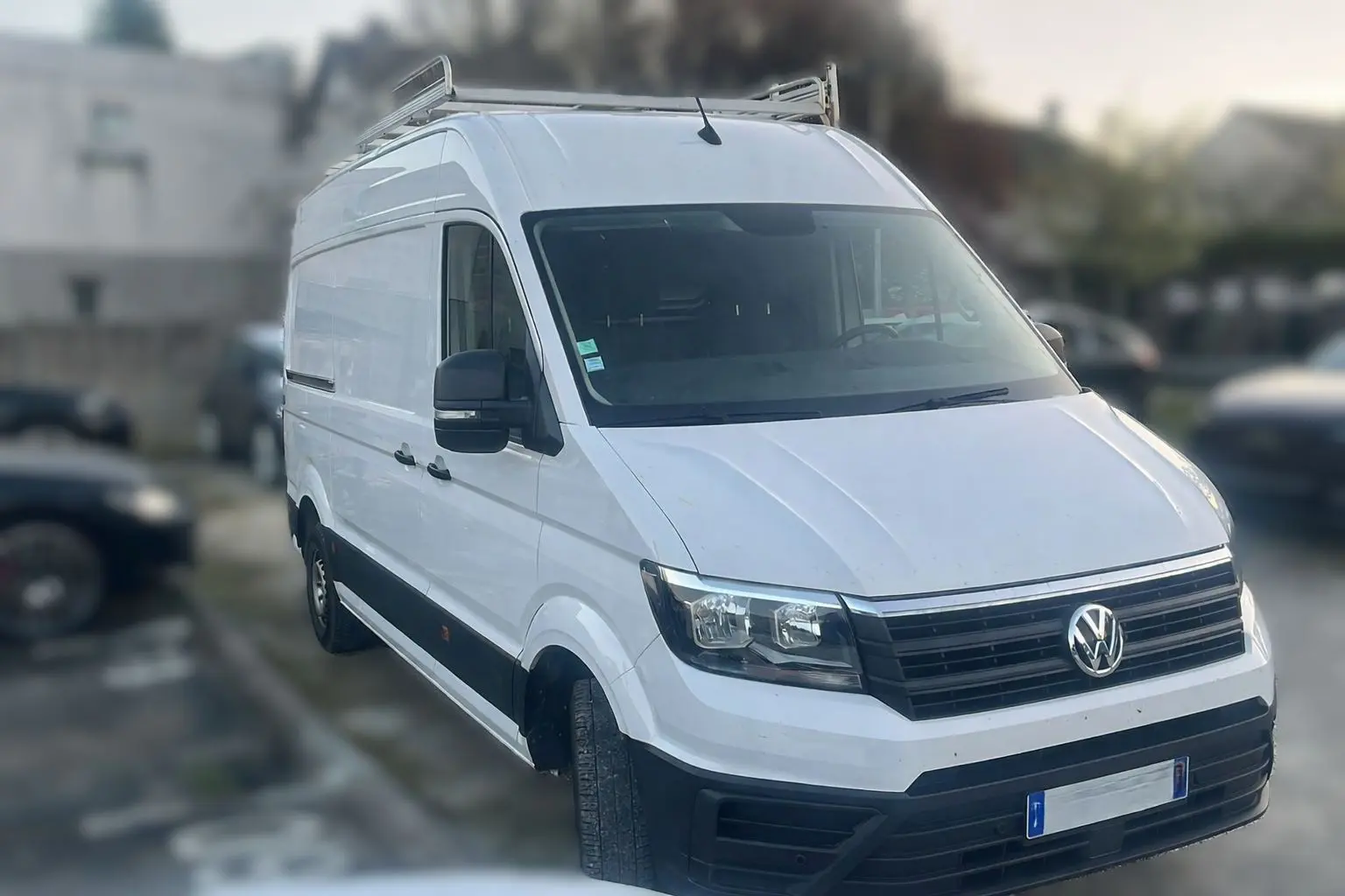Volkswagen Crafter blanc en 3/4 avant droit, fourgon utilitaire avec galerie de toit et rétroviseurs noirs.