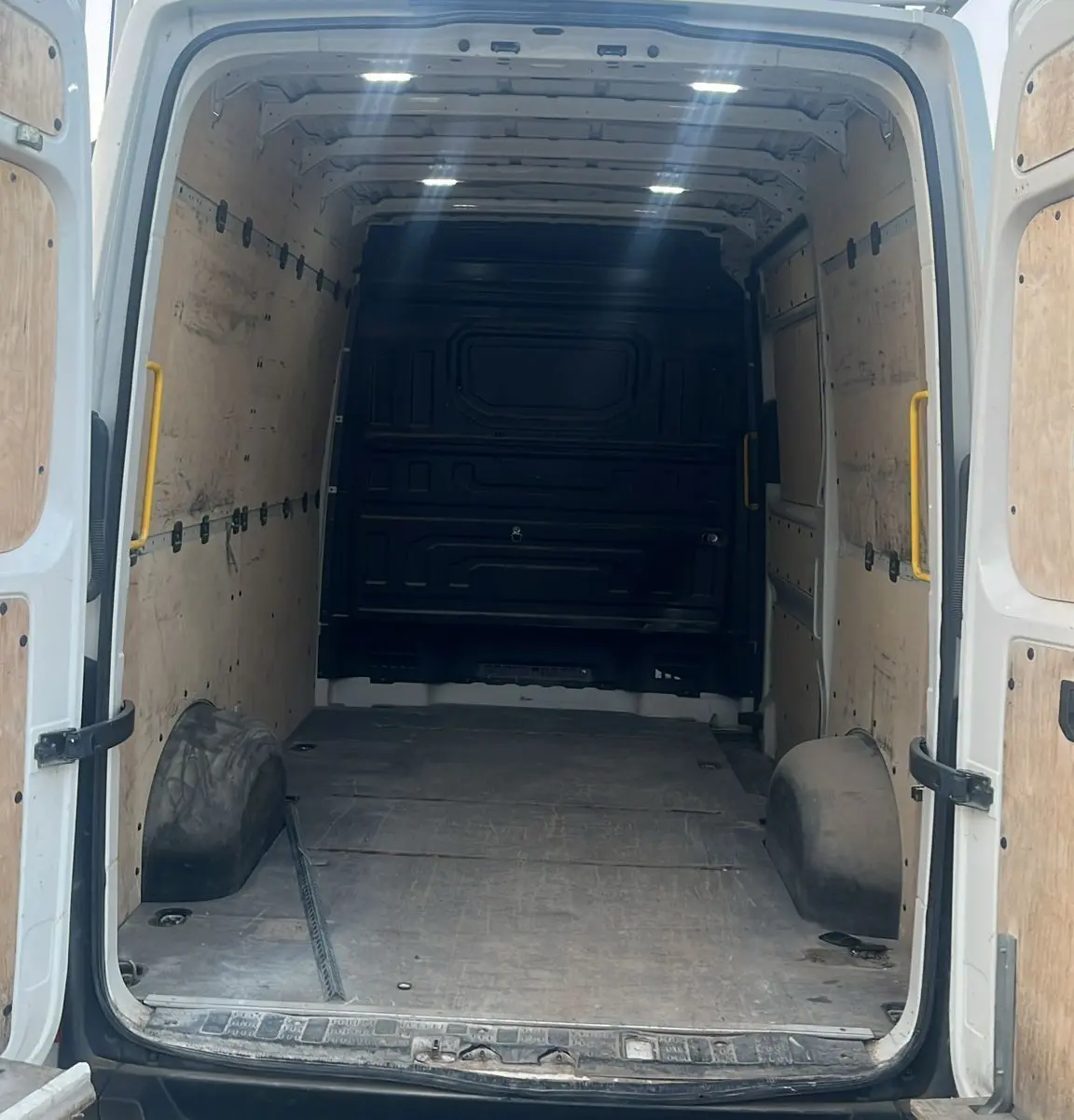 Vue arrière ouverte du Volkswagen Crafter blanc montrant l'intérieur vide et le plancher renforcé avec hayon et attelage.