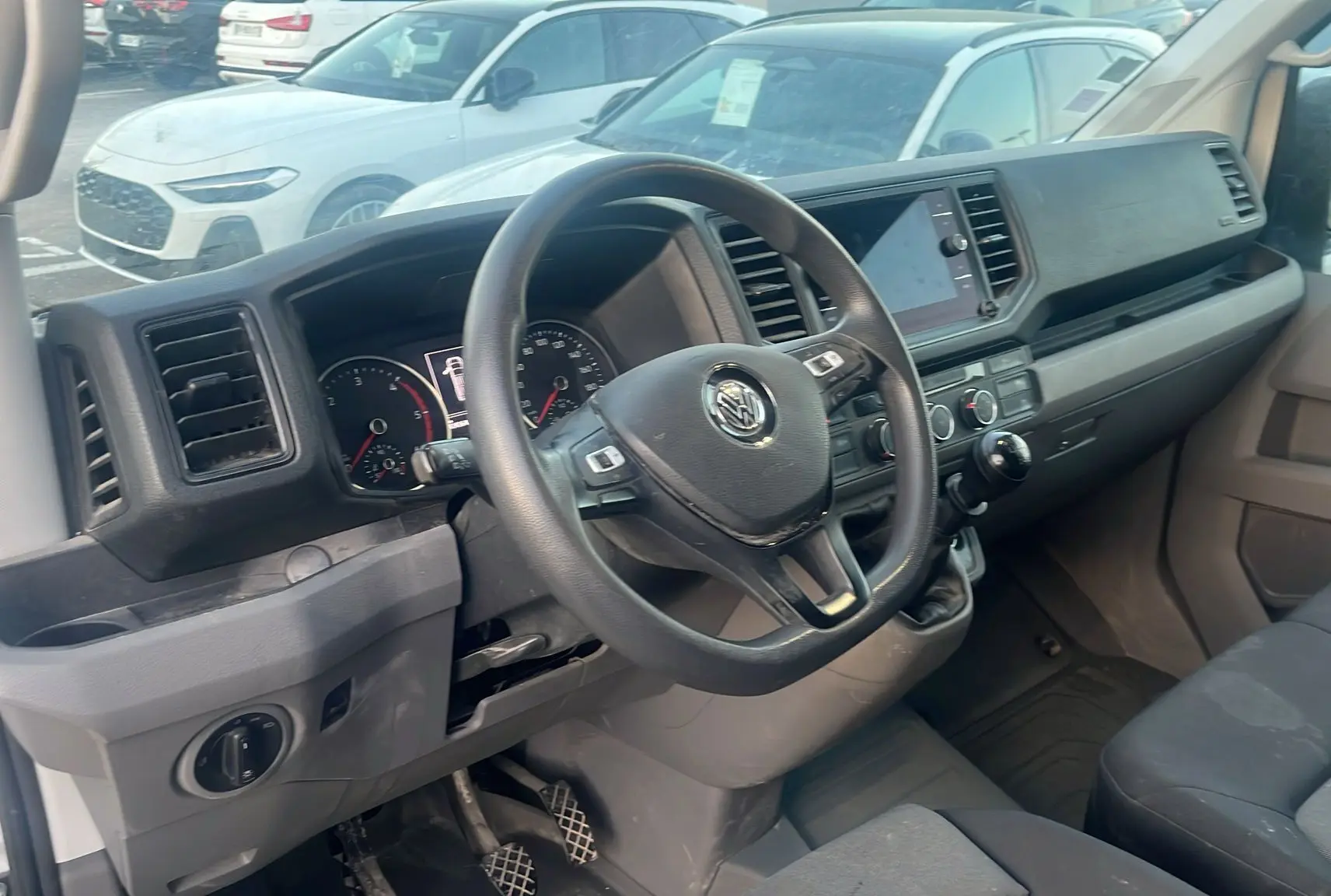 Vue intérieure côté conducteur du Volkswagen Crafter blanc, montrant le volant multifonctions et la console centrale.