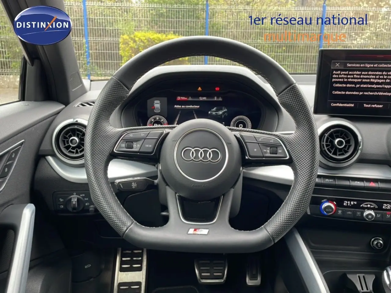 Vue intérieure centrée sur le volant noir perforé de l'Audi Q2 35 2.0 TDI S-Line avec tableau de bord digital et aérateurs ronds.