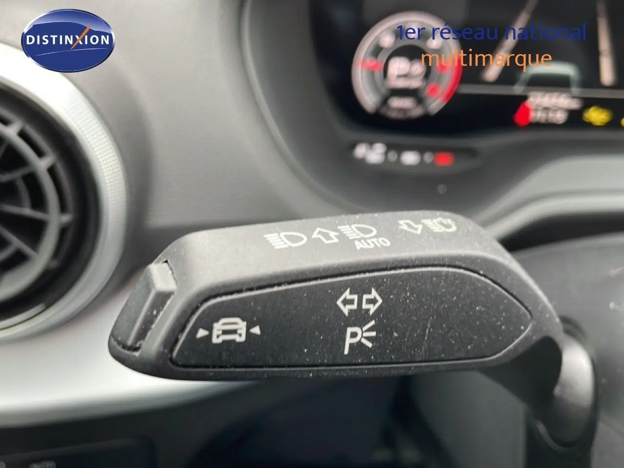 Gros plan sur la manette de clignotant et feux d'un Audi Q2 noir mito metal, intérieur avec tableau de bord flou en arrière-plan.
