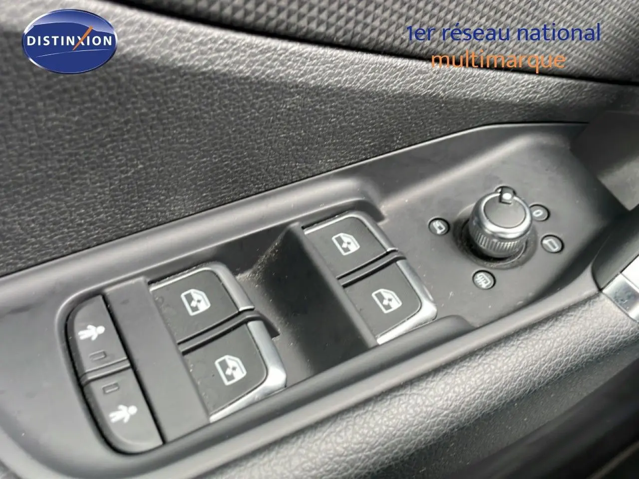 Gros plan sur les commandes de lève-vitres et réglage des rétroviseurs côté conducteur d'un Audi Q2 noir mito metal.