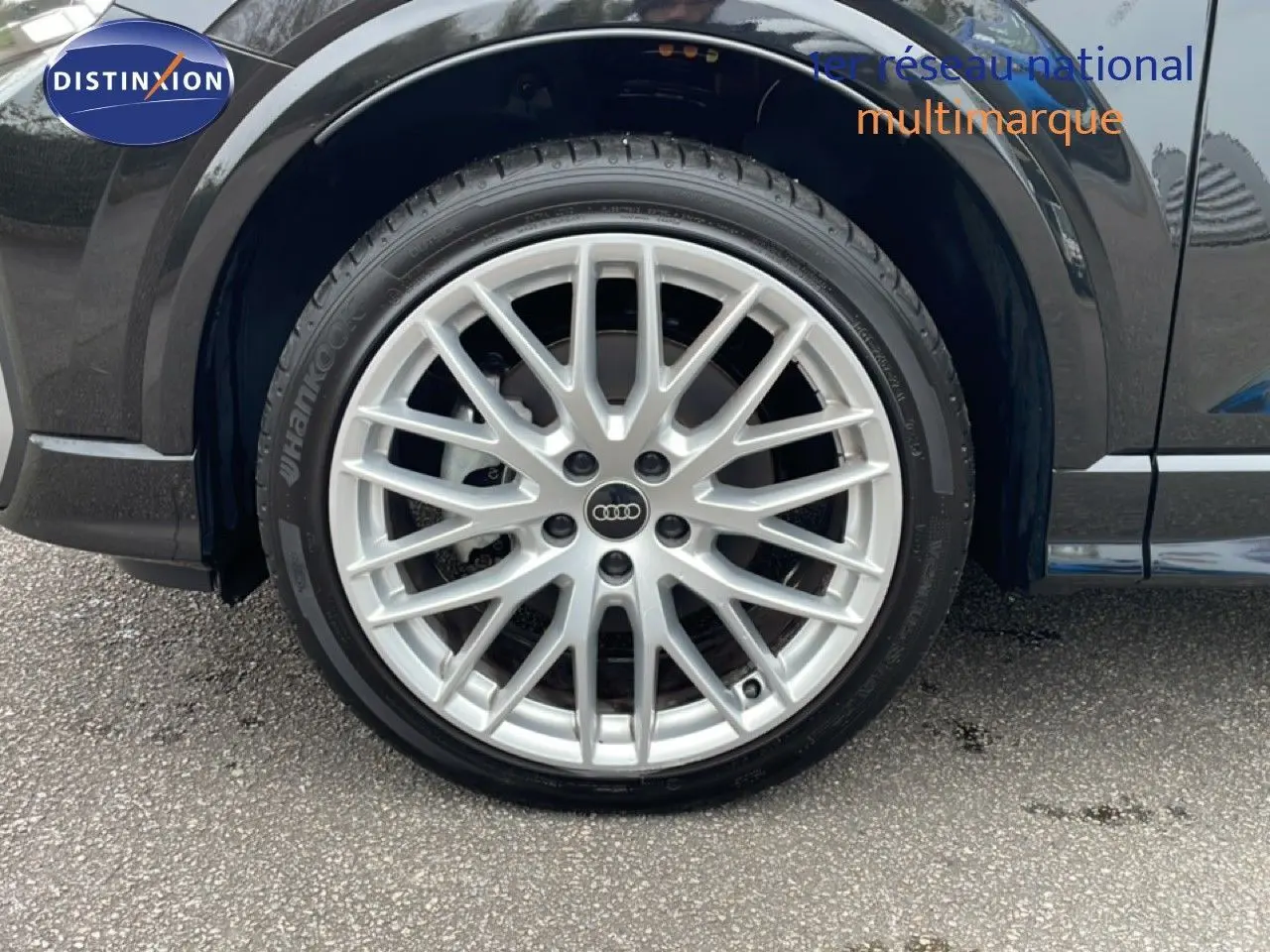 Gros plan sur la roue avant gauche d’un Audi Q2 noir mito metal avec jante alliage argentée multi-branches.
