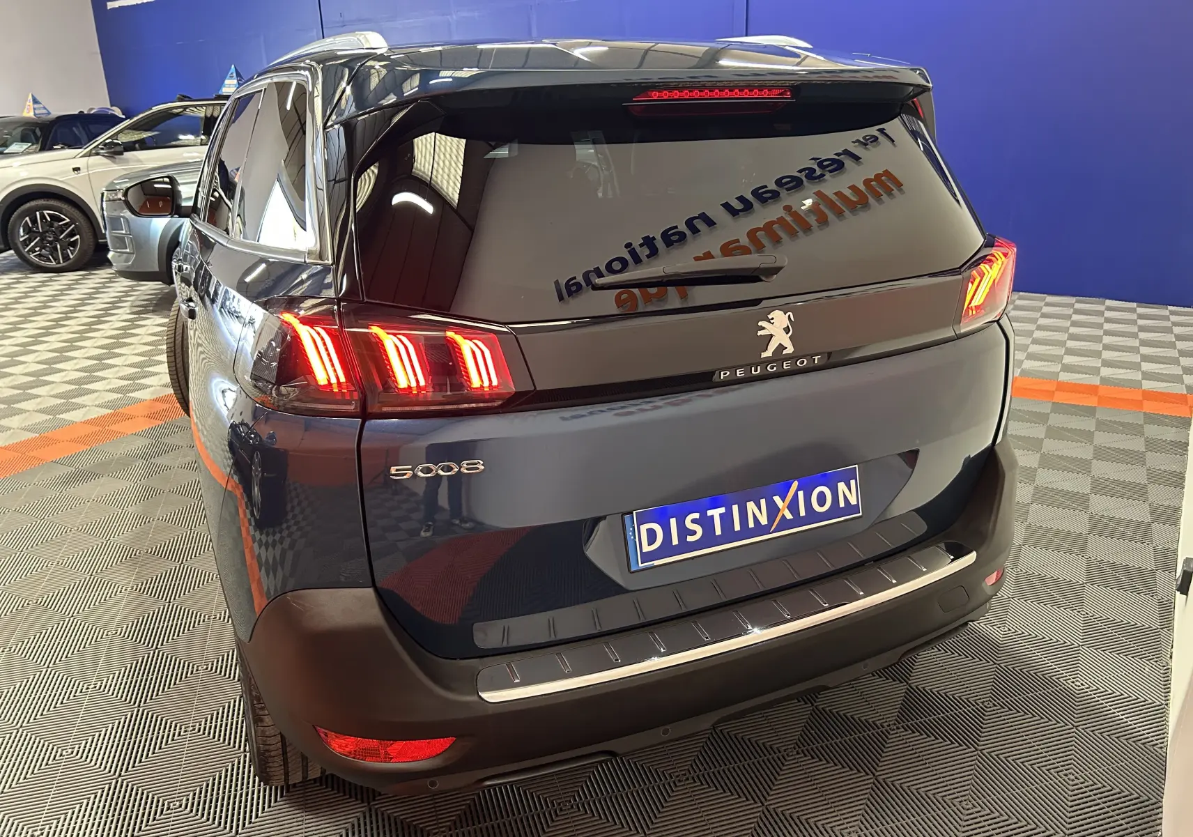 Vue 3/4 arrière droite d’un Peugeot 5008 Bleu Célèbes avec feux arrière LED allumés dans un showroom.