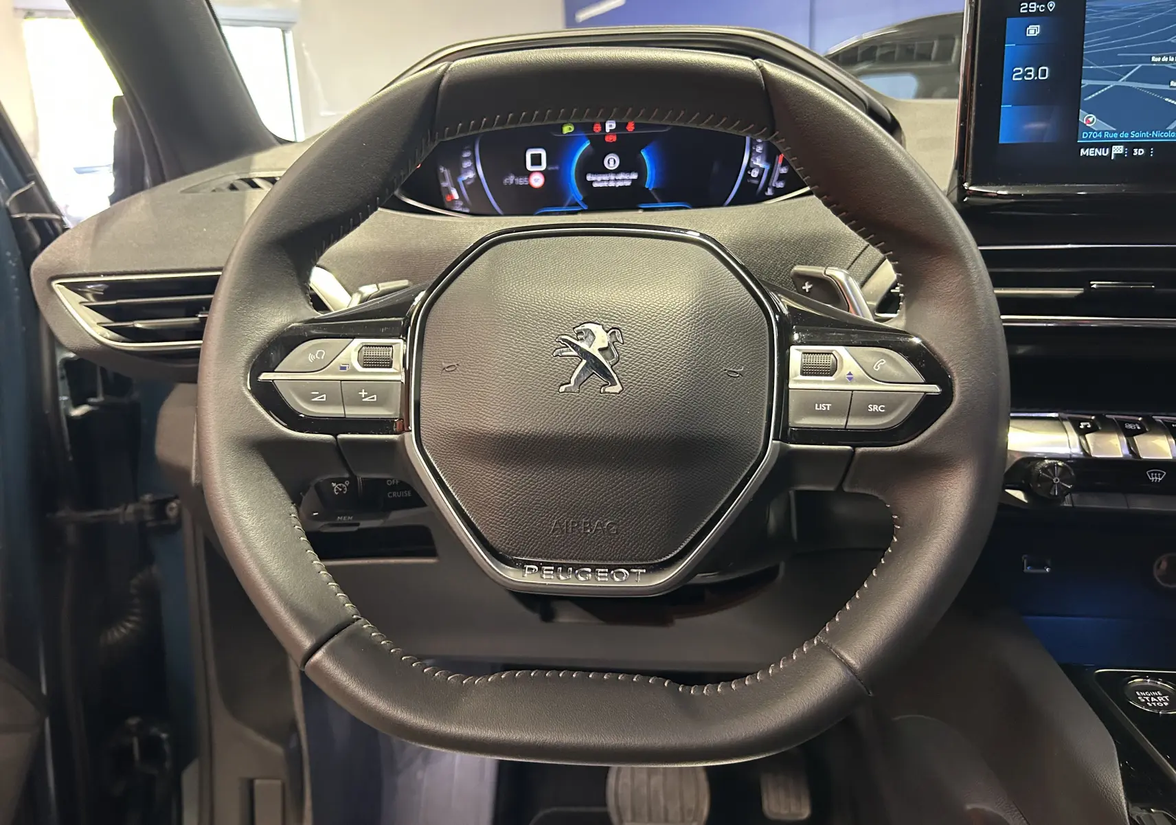 Vue rapprochée du volant noir du Peugeot 5008 2024, avec commandes intégrées et tableau de bord numérique en arrière-plan.