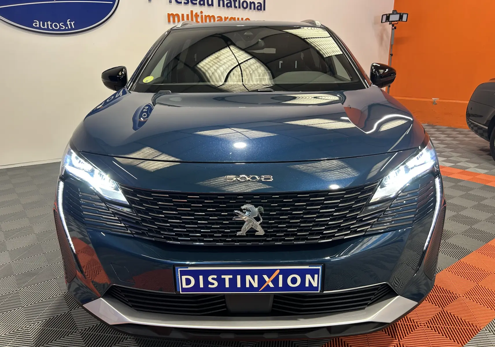Vue avant frontale du Peugeot 5008 bleu Célèbes avec calandre noire et phares LED allumés en showroom.