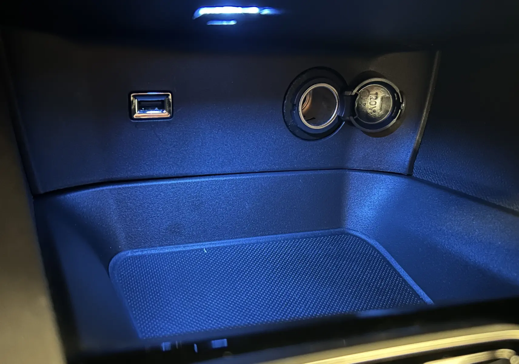 Prise USB et allume-cigare éclairés en bleu dans le compartiment central d’un Peugeot 5008 2024.