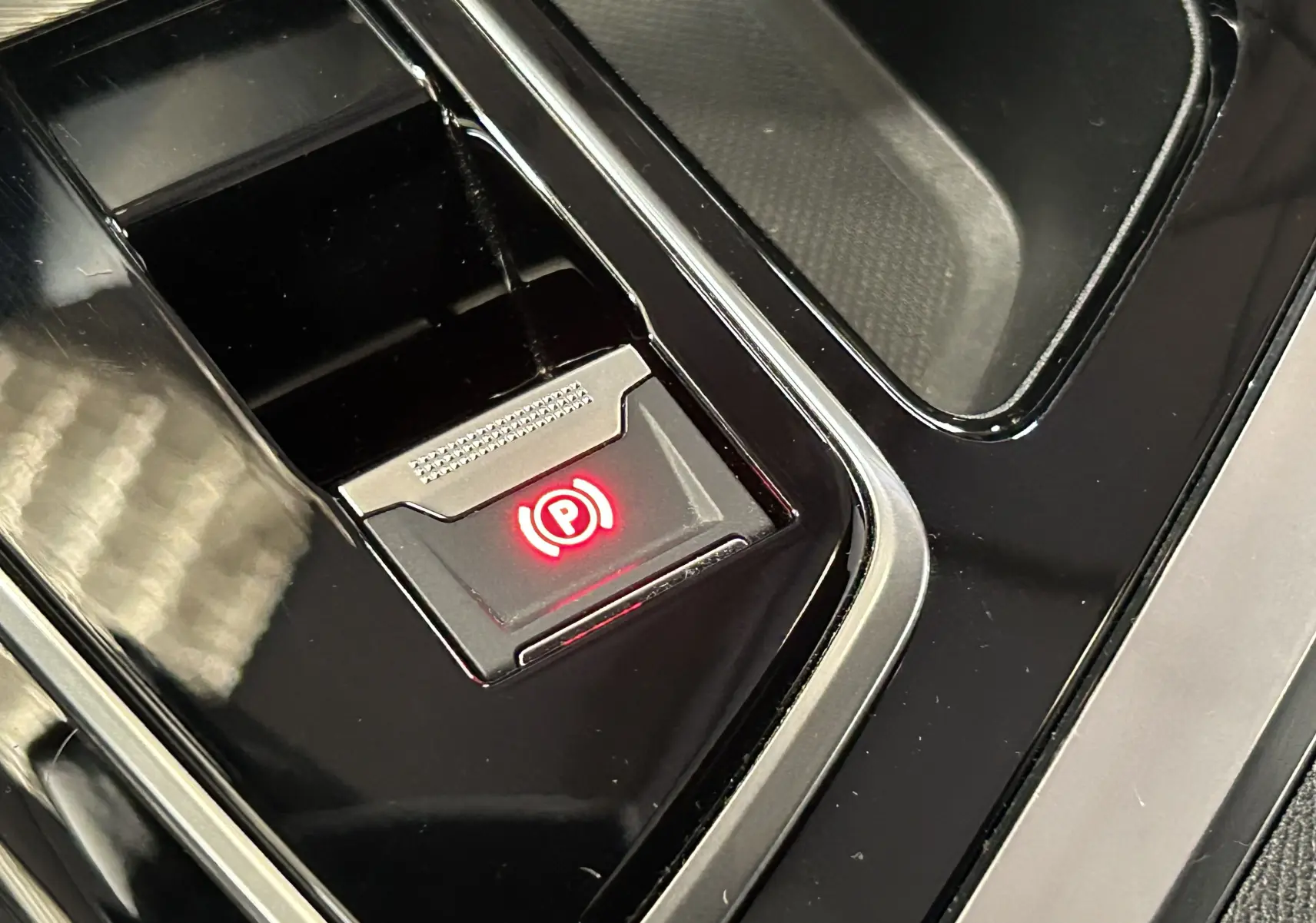 Gros plan sur le bouton de frein à main électronique rouge dans la console centrale noire du Peugeot 5008 2024.