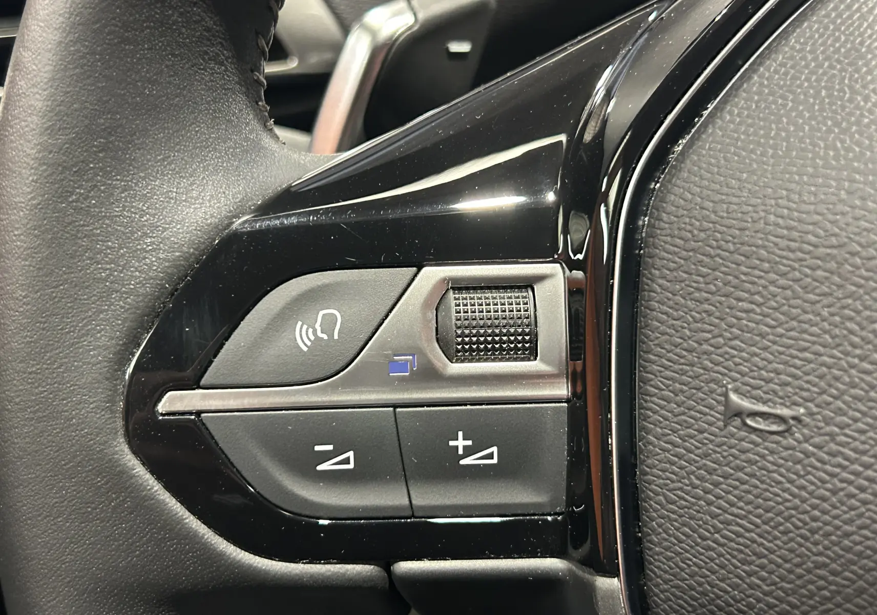 Gros plan sur les commandes du volant côté gauche du Peugeot 5008 2024, finition noire brillante avec boutons de volume et commande vocale.
