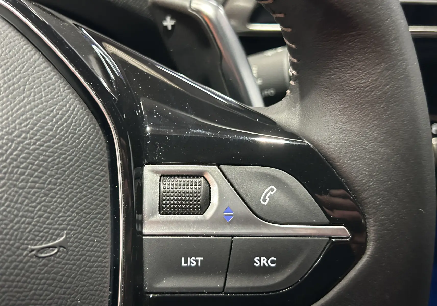 Gros plan sur les commandes multifonctions noires du volant côté gauche du Peugeot 5008 Bleu Célèbes 2024.