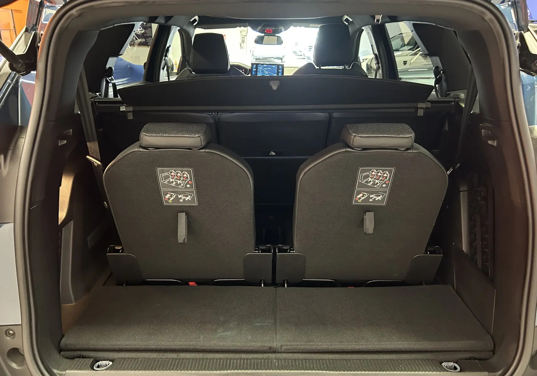 Vue arrière du coffre ouvert du Peugeot 5008 bleu Célèbes, montrant les sièges arrière relevés et la tablette cache-bagages.
