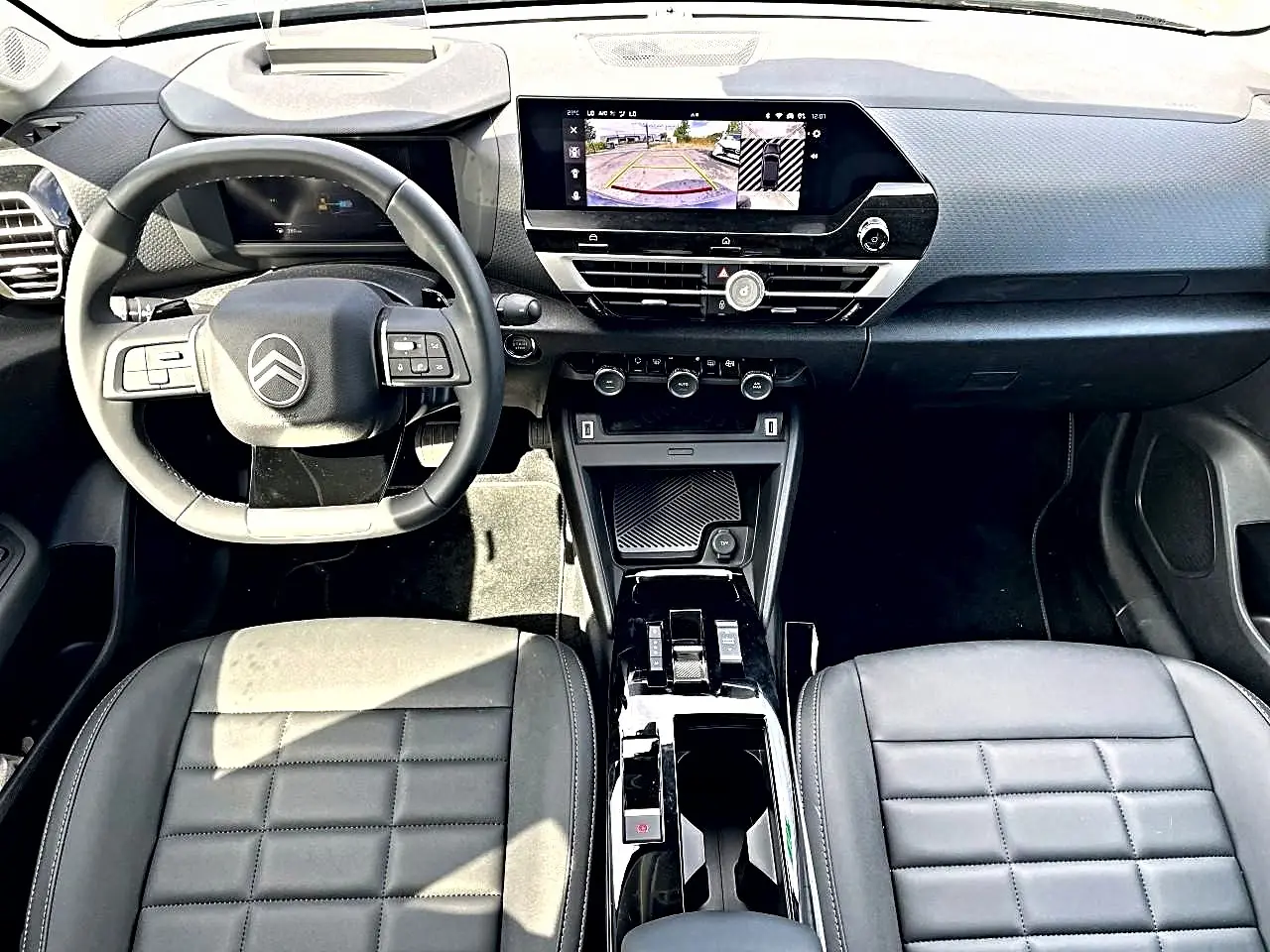 Vue intérieure avant du tableau de bord et volant cuir noir du Citroën C4 X 1.2 hybride avec écran tactile et caméra de recul affichée.