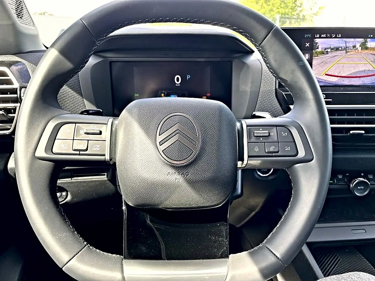 Vue rapprochée du volant cuir noir de la Citroën C4 X 2025 avec commandes intégrées et écran tactile de caméra de recul visible.