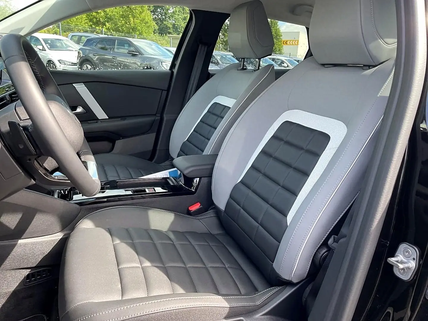 Vue intérieure côté conducteur de la Citroën C4 X noire 2025, sièges bi-matière gris et noir avec accoudoir central.