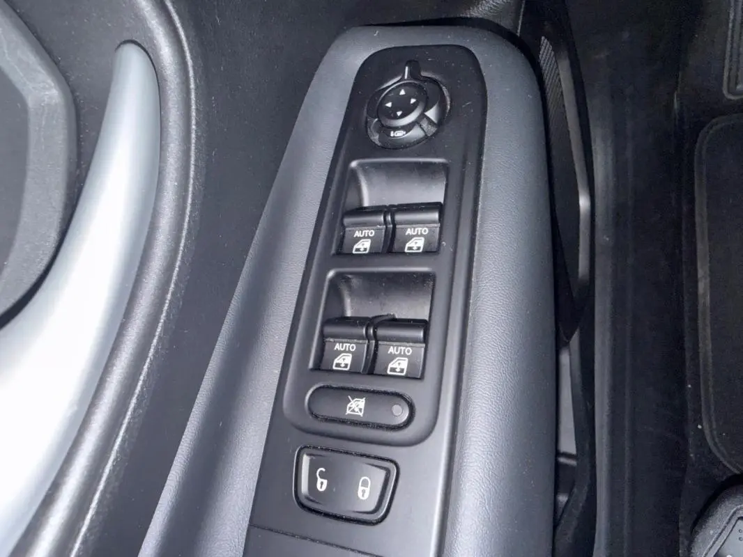 Gros plan sur les commandes des vitres électriques et rétroviseurs côté conducteur du Jeep Renegade gris anthracite 2024.