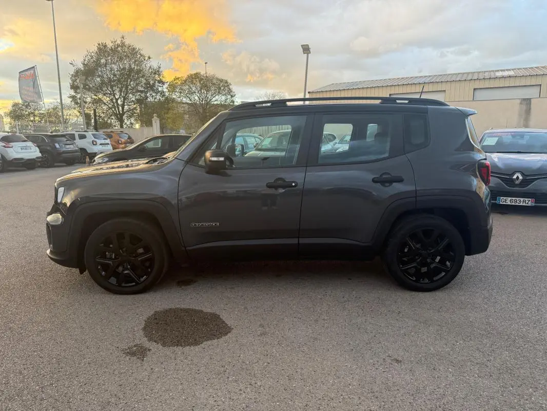 Profil côté droit d'un Jeep Renegade gris anthracite 2024 avec jantes alliage noires et barres de toit visibles.