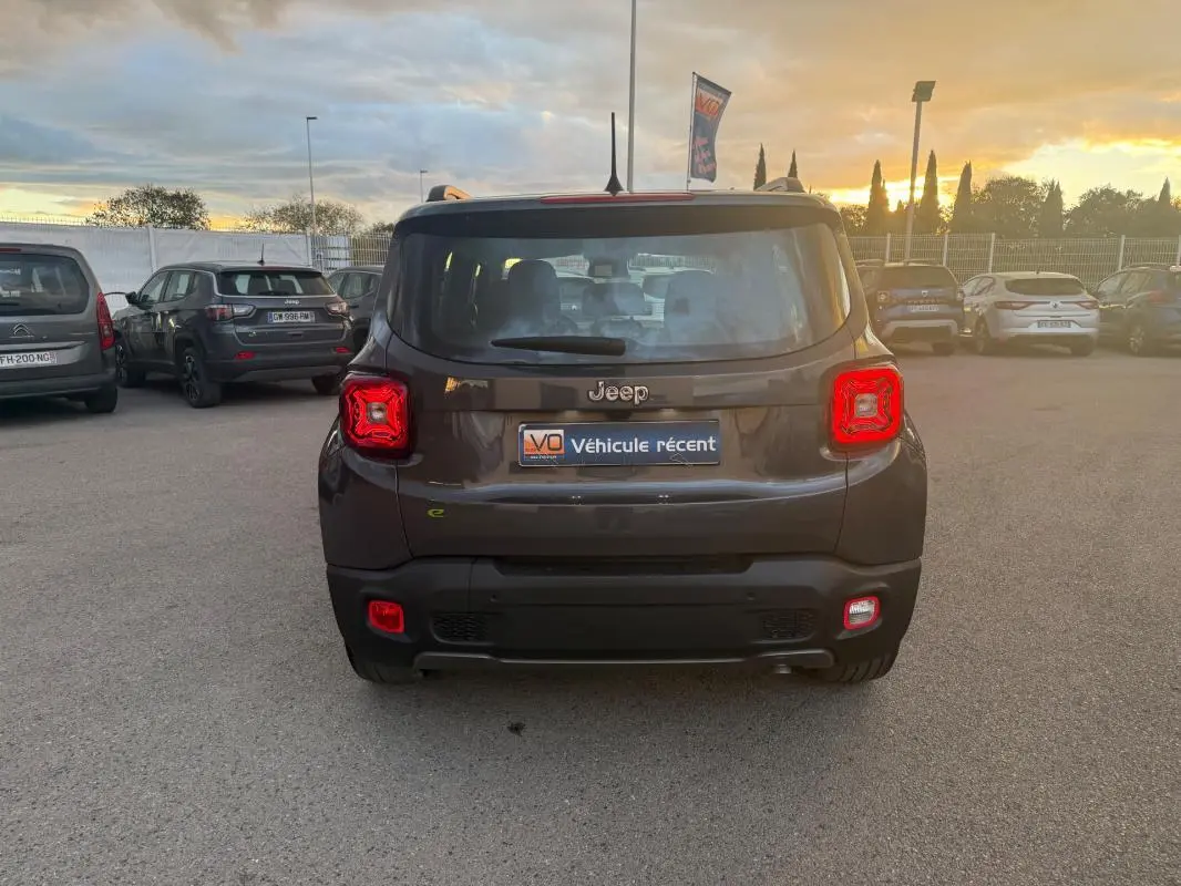 Vue arrière d'un Jeep Renegade gris anthracite 2024 avec feux arrière allumés et barres de toit visibles au coucher du soleil.