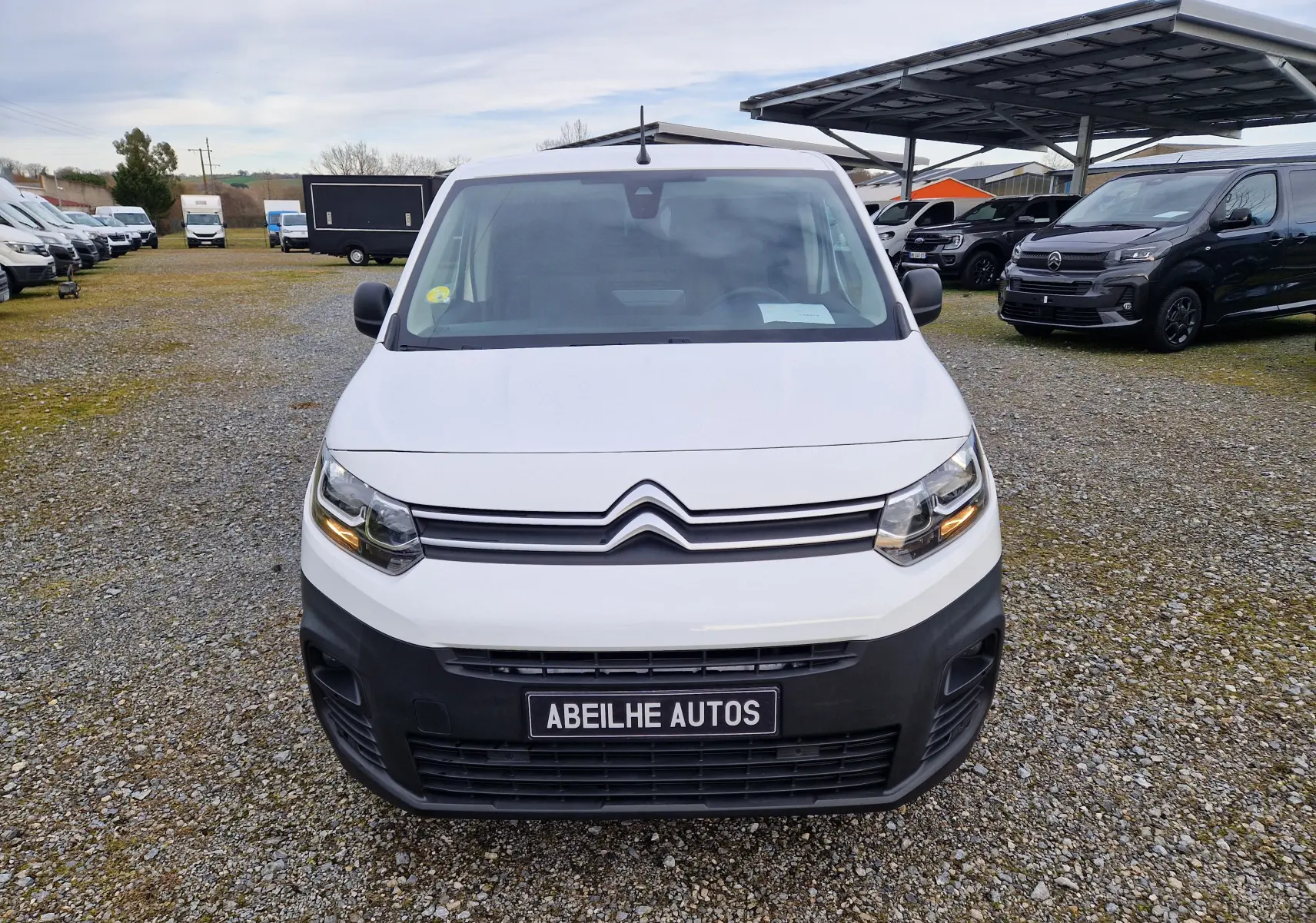 Vue frontale d’un Citroën Berlingo blanc 2021 avec calandre noire et plaque Abeilhe Autos sur un parking extérieur.