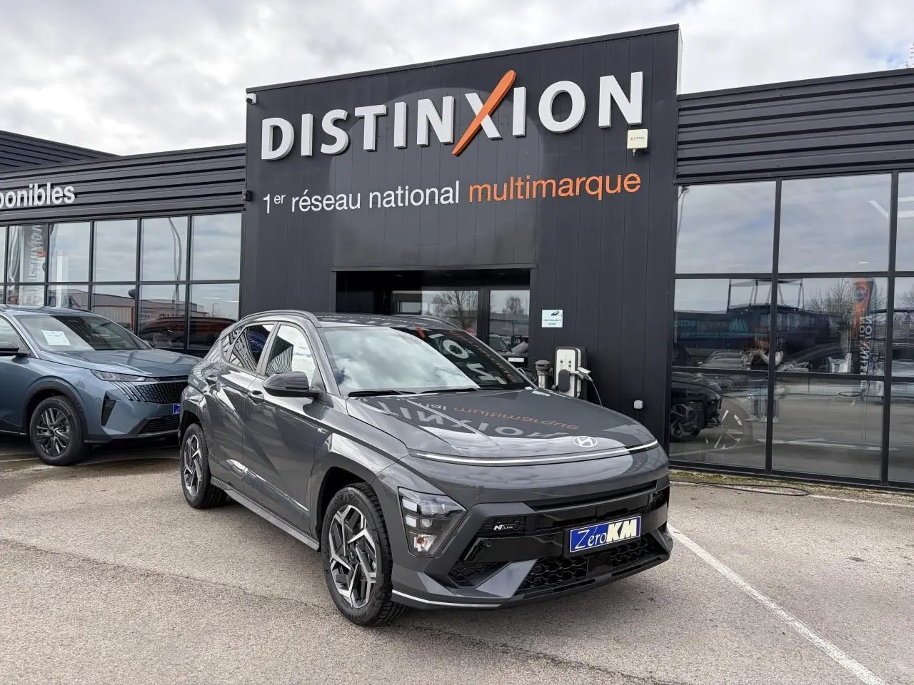 Hyundai KONA II 1.6 Hybrid N Line gris Ecotronic en 3/4 avant droit devant un showroom Distinxion.