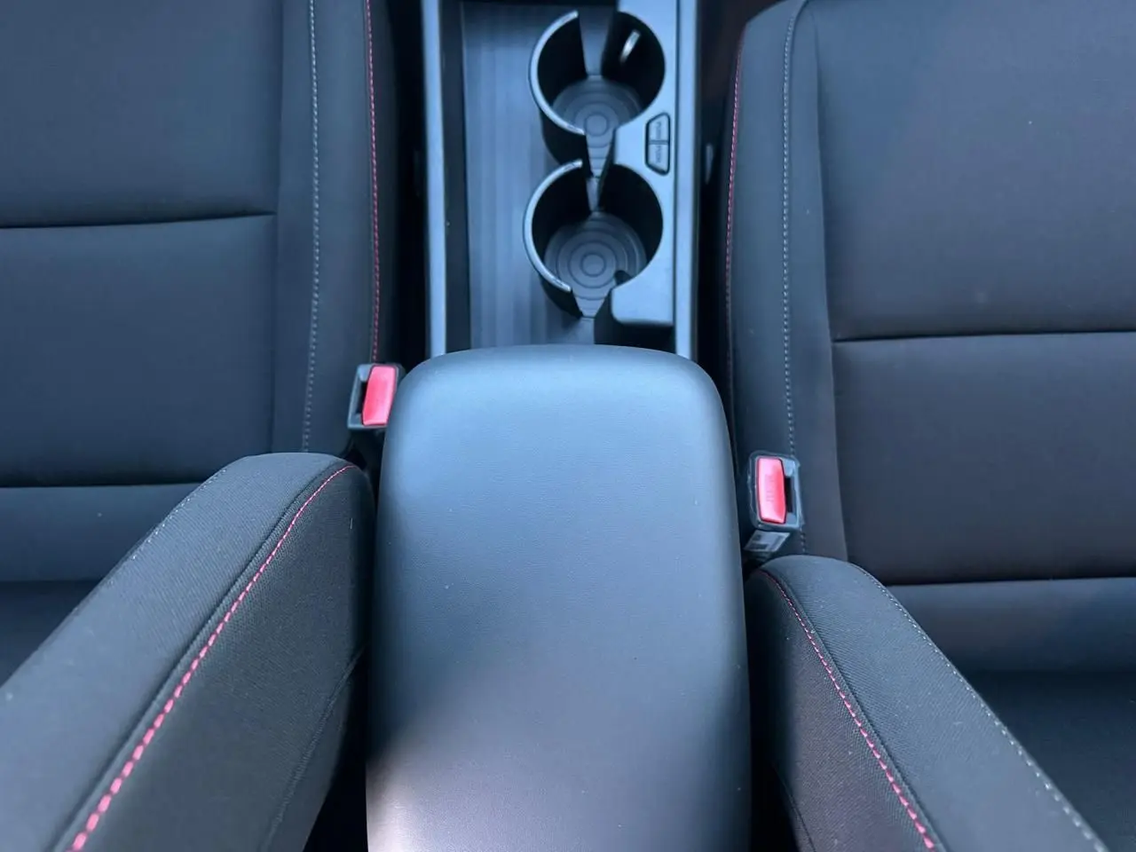 Vue plongeante sur l'accoudoir central noir et les sièges avant noirs avec surpiqûres rouges du Hyundai Kona 2026.