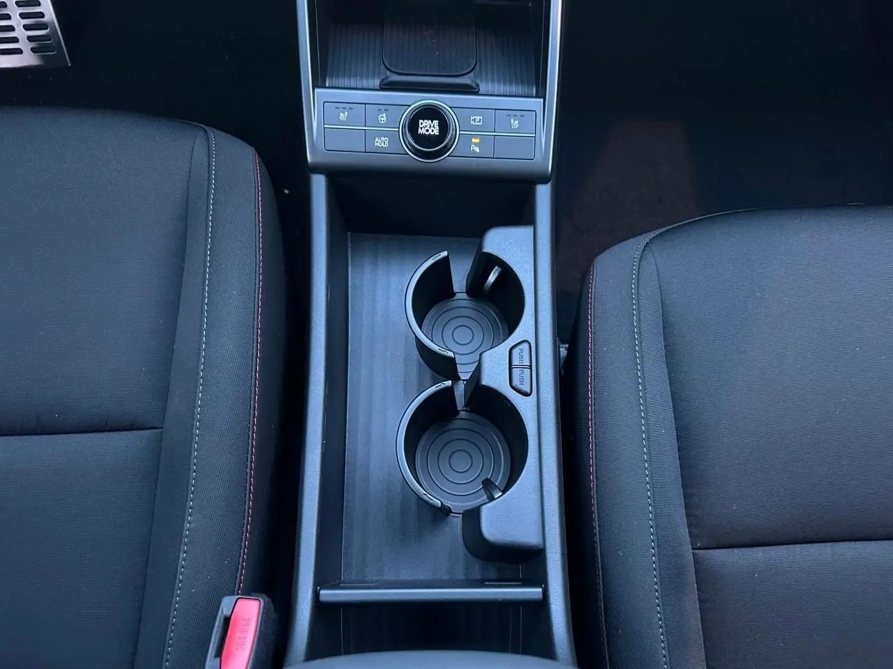 Vue plongeante sur la console centrale noire du Hyundai Kona 2026 avec porte-gobelets et commandes Drive Mode.