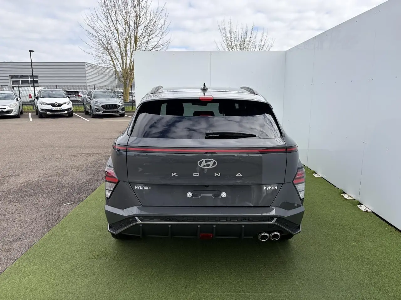 Vue arrière d'un Hyundai Kona 2 hybride gris métallisé avec feux arrière LED et double sortie d'échappement chromée.