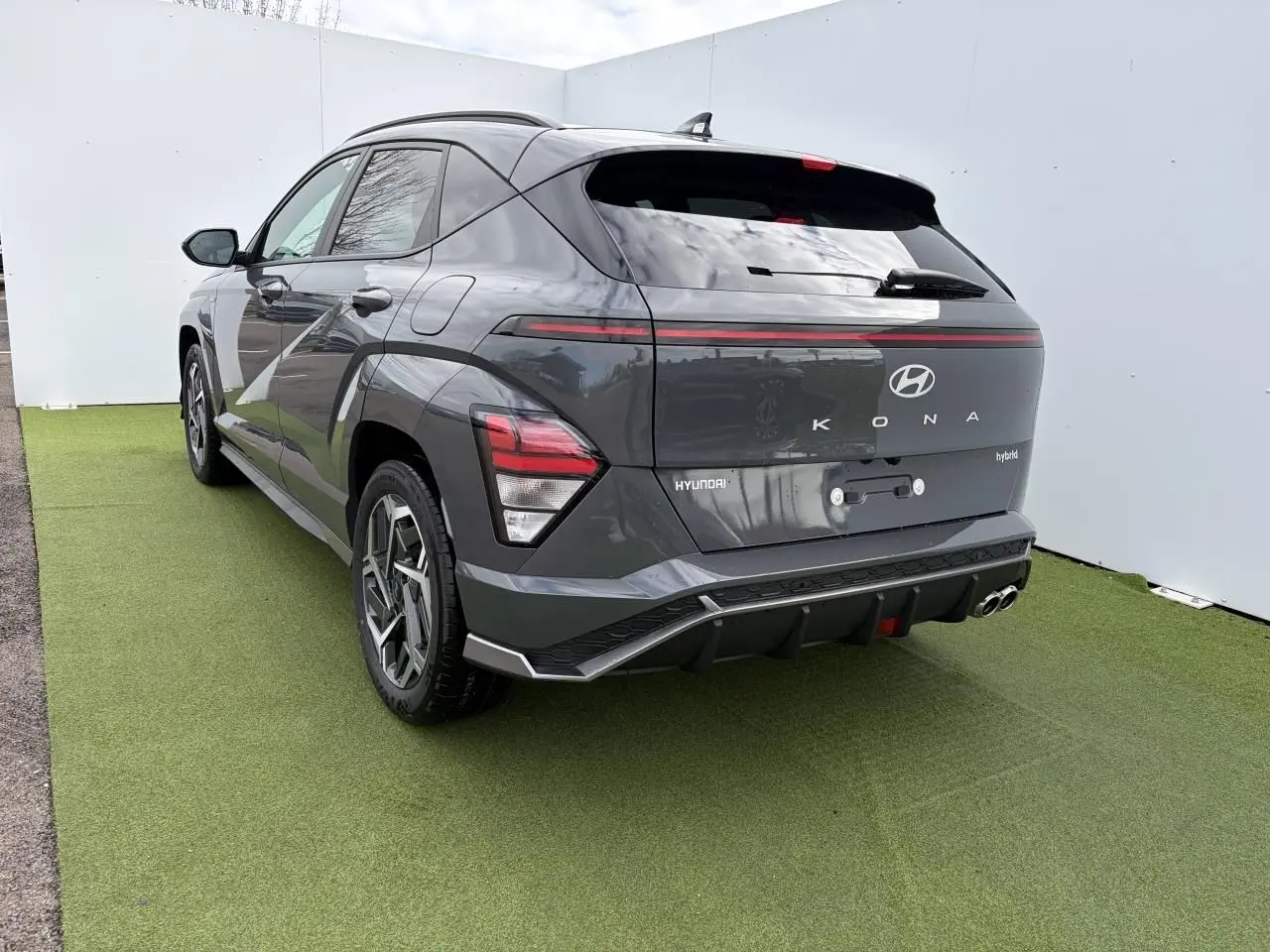 Vue 3/4 arrière droite du Hyundai KONA II hybride en gris métallisé Ecotronic, avec feux arrière LED et double sortie d'échappement.