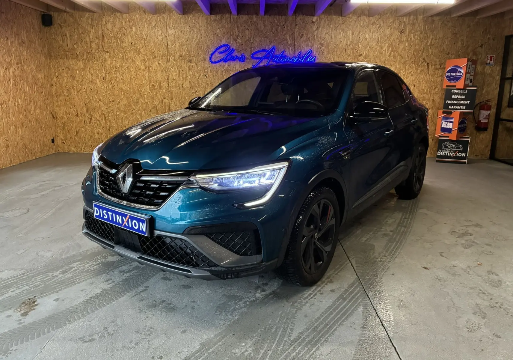 Renault Arkana bleu 3/4 avant droit en intérieur, avec calandre noire et phares LED allumés.