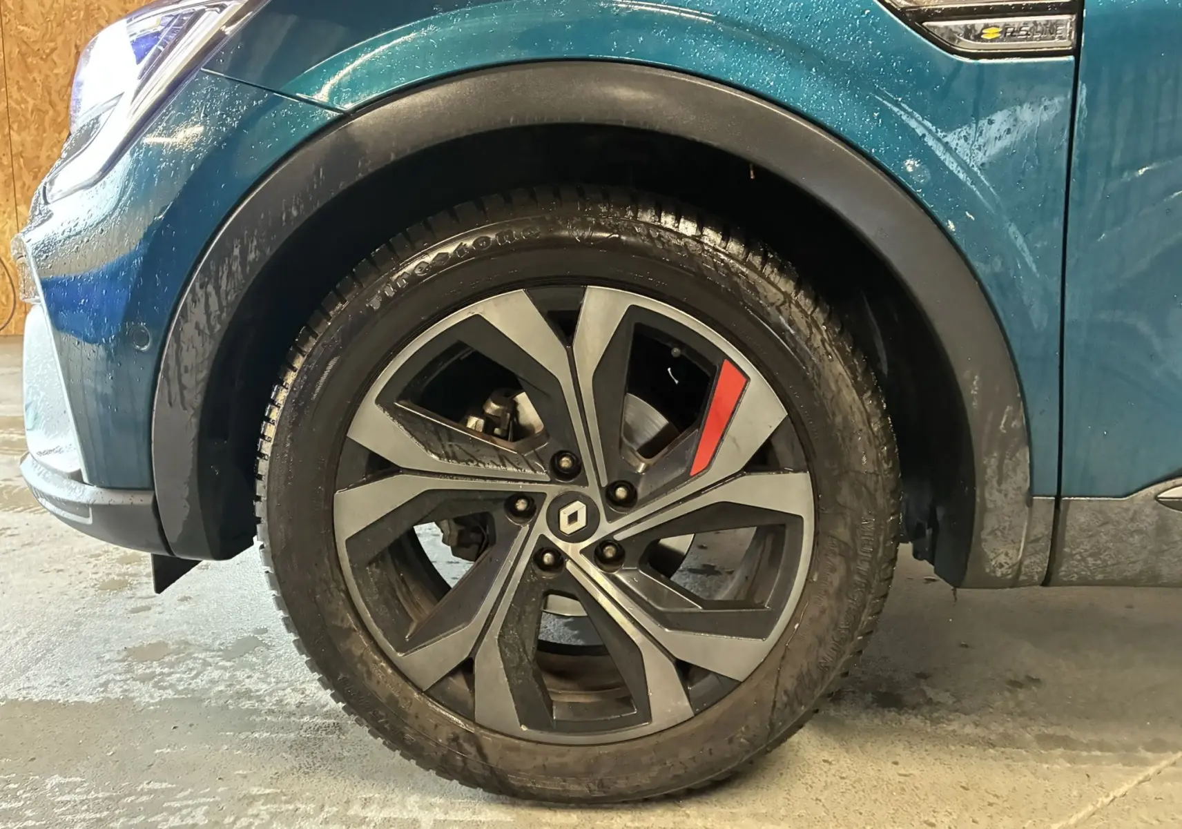 Gros plan sur la roue avant gauche d’un Renault Arkana bleu 2021 avec jante alliage noire et détail rouge RS-Line.