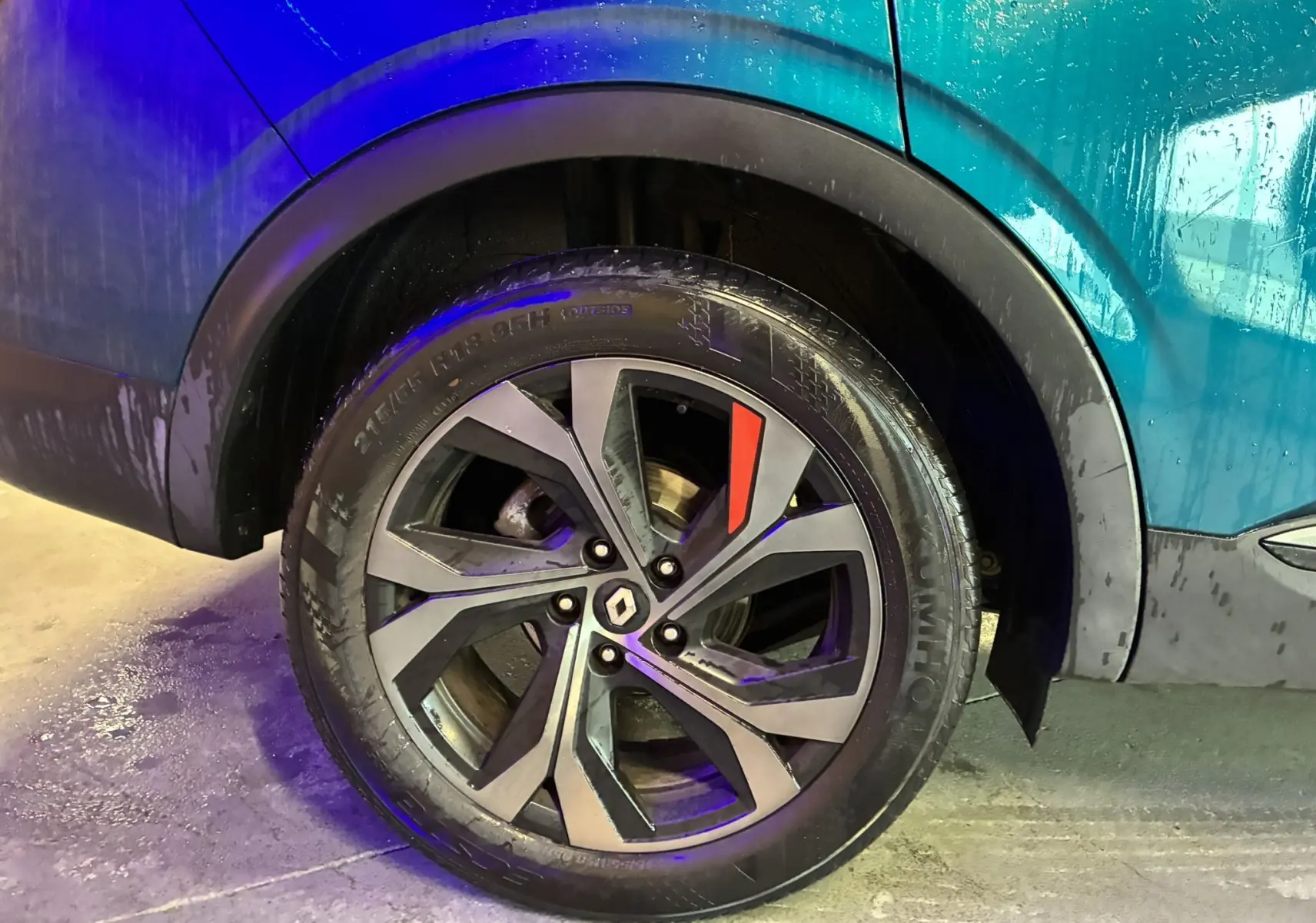 Gros plan sur la roue arrière droite d’un Renault Arkana bleu 2021 avec jante alliage à design noir et gris et détail rouge.