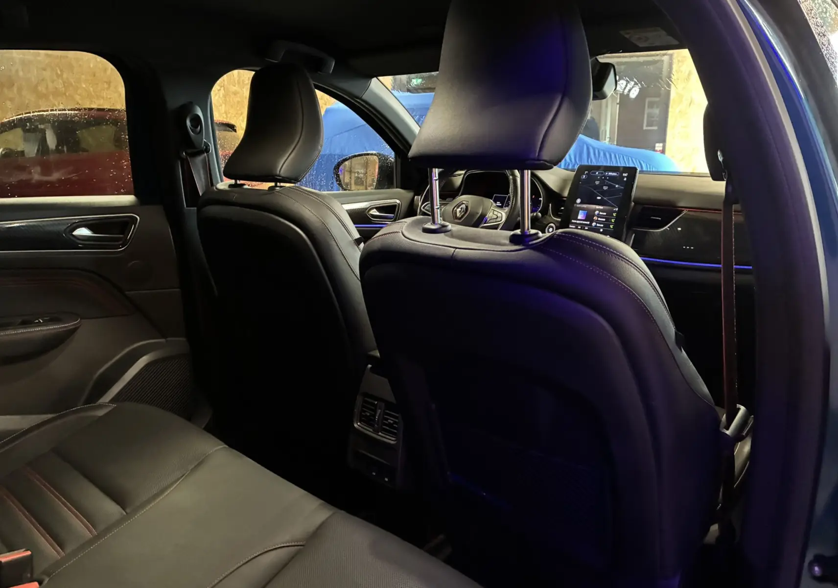 Vue intérieure arrière côté gauche du Renault Arkana bleu 2021, mettant en valeur les sièges en cuir noir et l'écran tactile central.