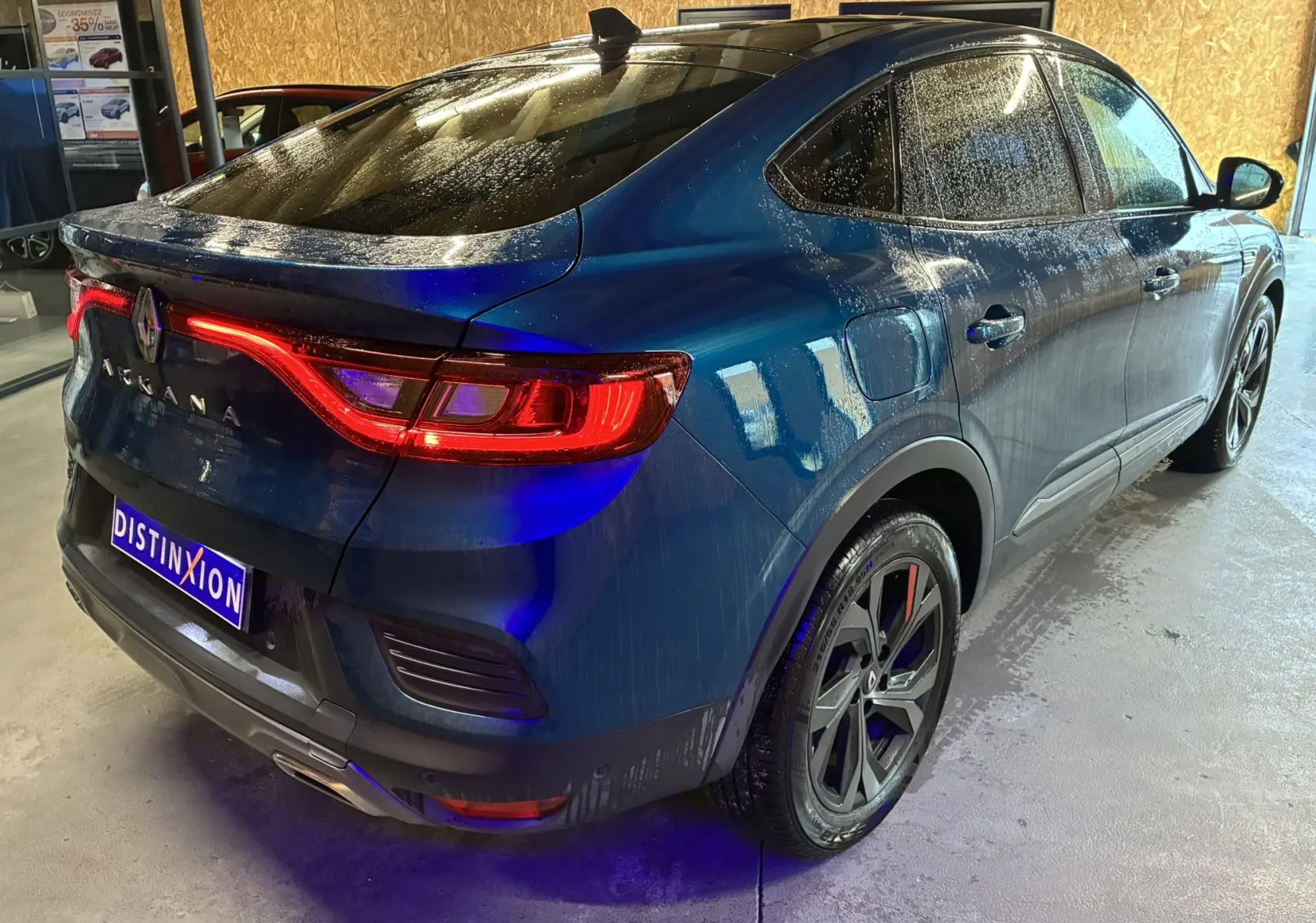 Vue 3/4 arrière droite d'une Renault Arkana bleu 2021 avec feux arrière allumés et jantes noires distinctives.