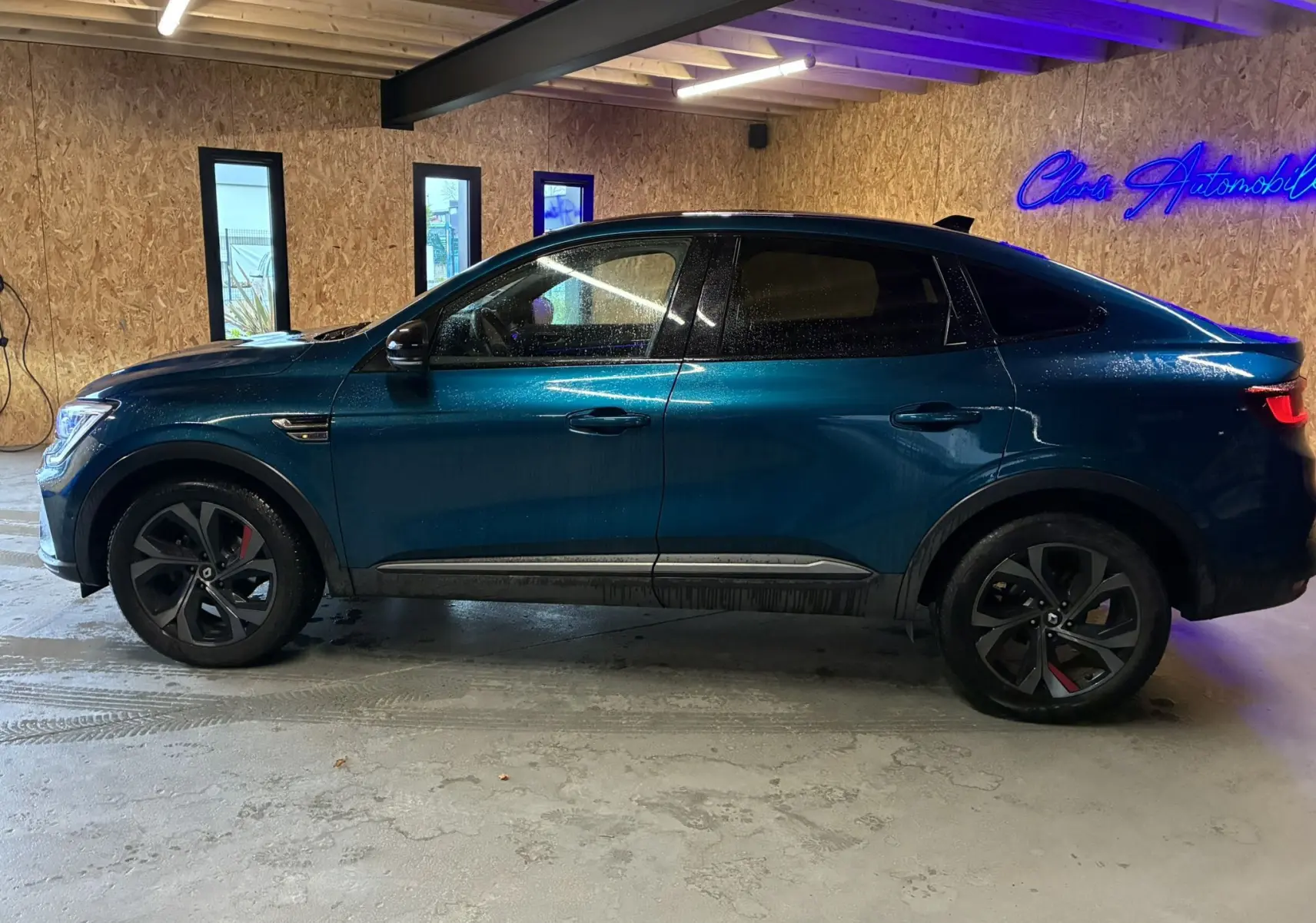 Vue de profil côté gauche d'un Renault Arkana 1.3 TCE 140 RS-Line bleu, avec jantes noires et étriers rouges, en intérieur.