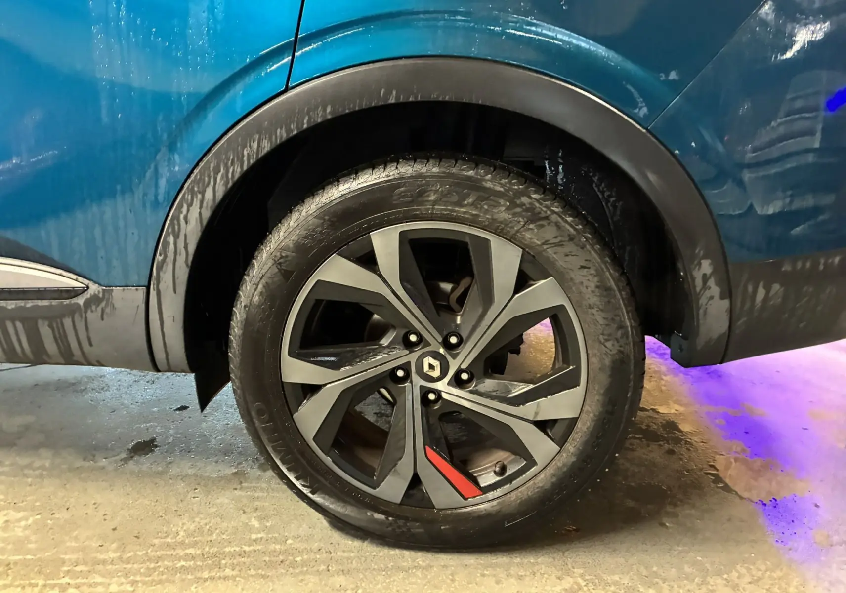 Gros plan sur la roue arrière gauche d’un Renault Arkana bleu 2021 avec jante noire et détail rouge RS-Line.