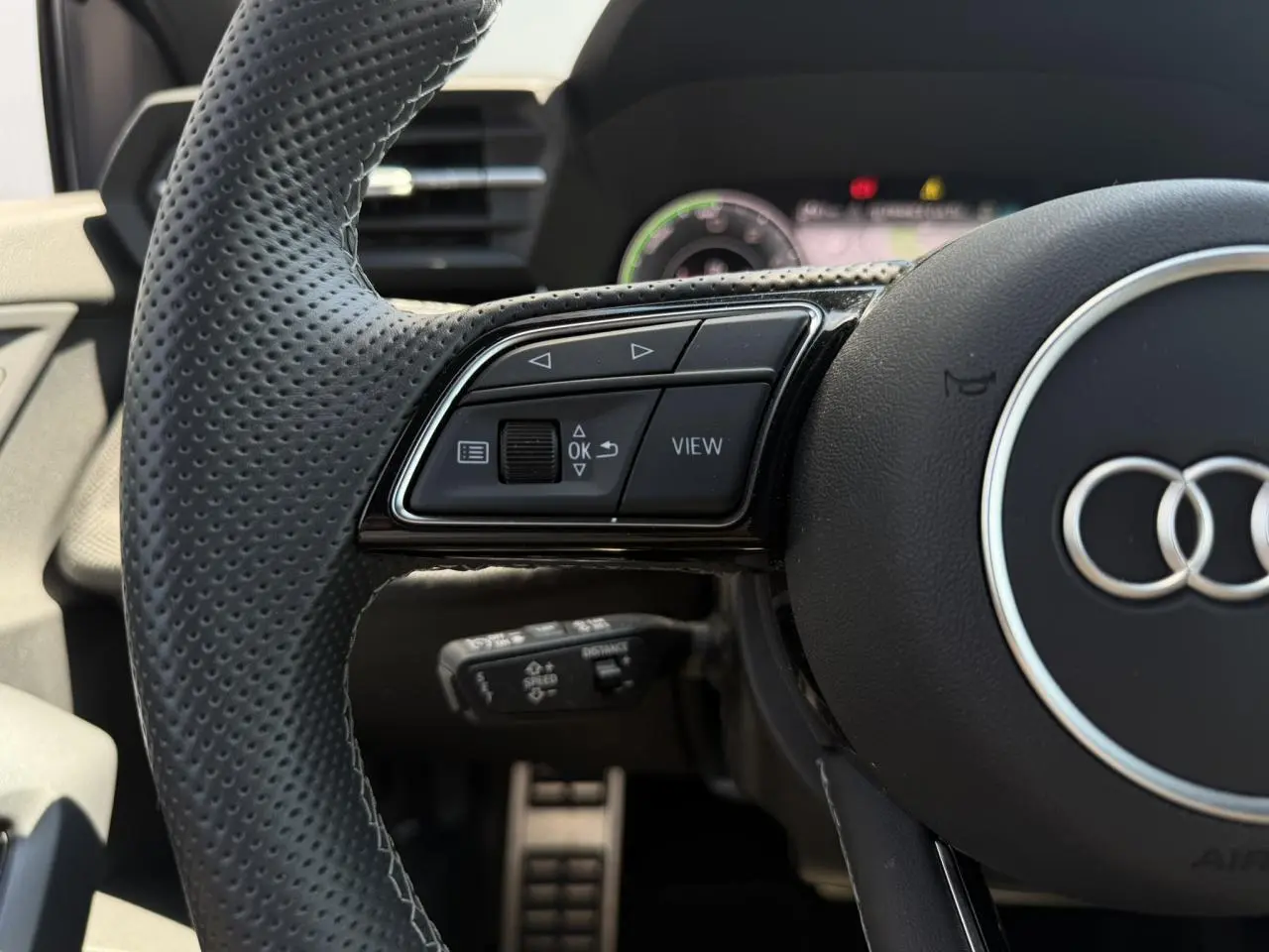 Gros plan sur le volant perforé noir de l'Audi A3 Sportback 2025 avec commandes multifonctions et logo Audi central.